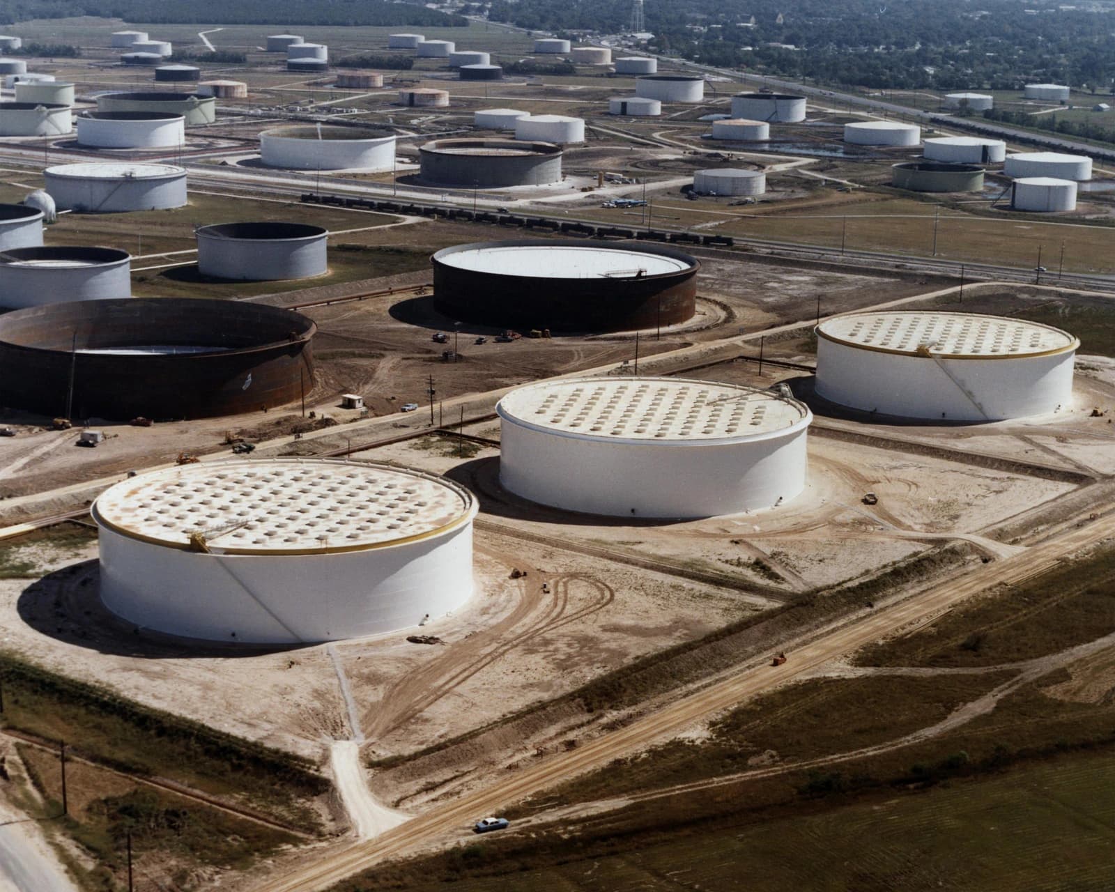 Aerial view of numerous large cylindrical crude oil storage tanks at a facility.