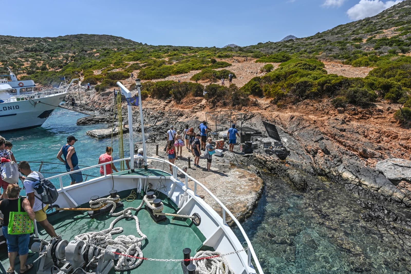 Tourists disembarking from a boat onto a rocky shore on Spinalonga Peninsula, Crete, Greece.