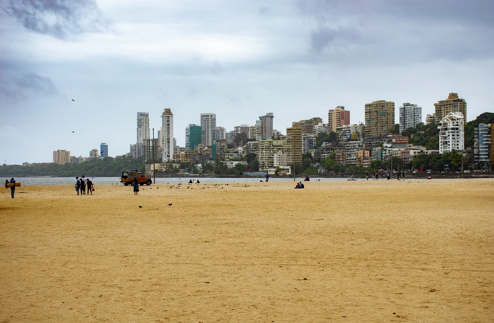 Skyline of tall buildings rising behind a wide sandy beach in Mumbai, India.
