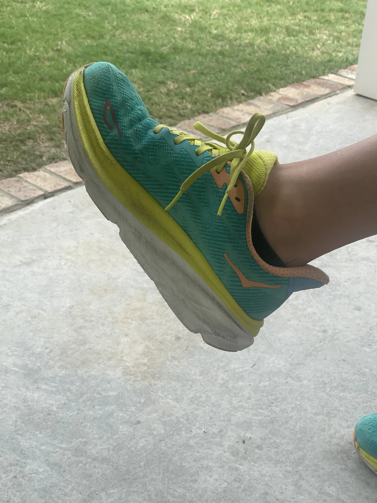 A person's foot wearing a teal and yellow Hoka running shoe.