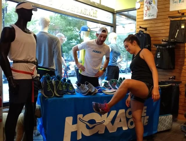 Man and woman interact near a display of Hoka running shoes.