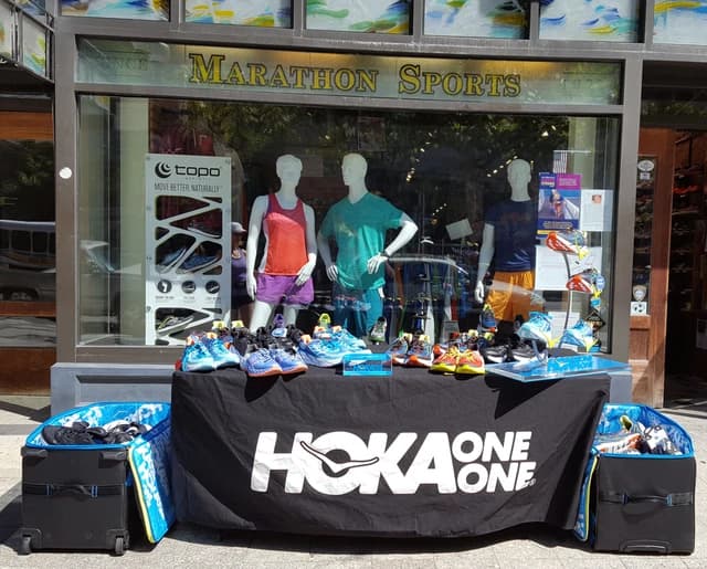 Hoka One One running shoes displayed on a table outside a Marathon Sports store.