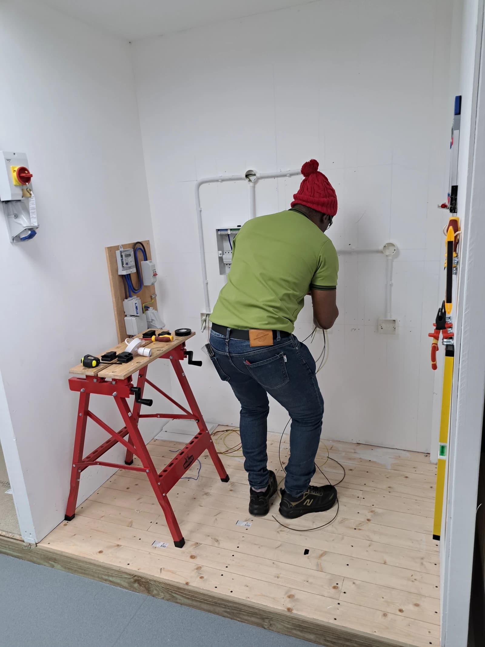 Electrician installing wiring in a white room with various electrical components.