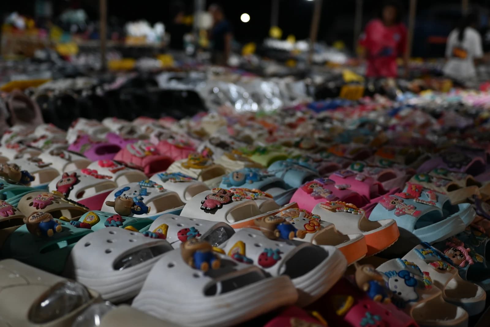 Colorful children's sandals and clogs with cartoon decorations displayed on a market table.
