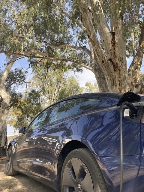 Blue Tesla Model 3 electric vehicle charging at an outdoor station.