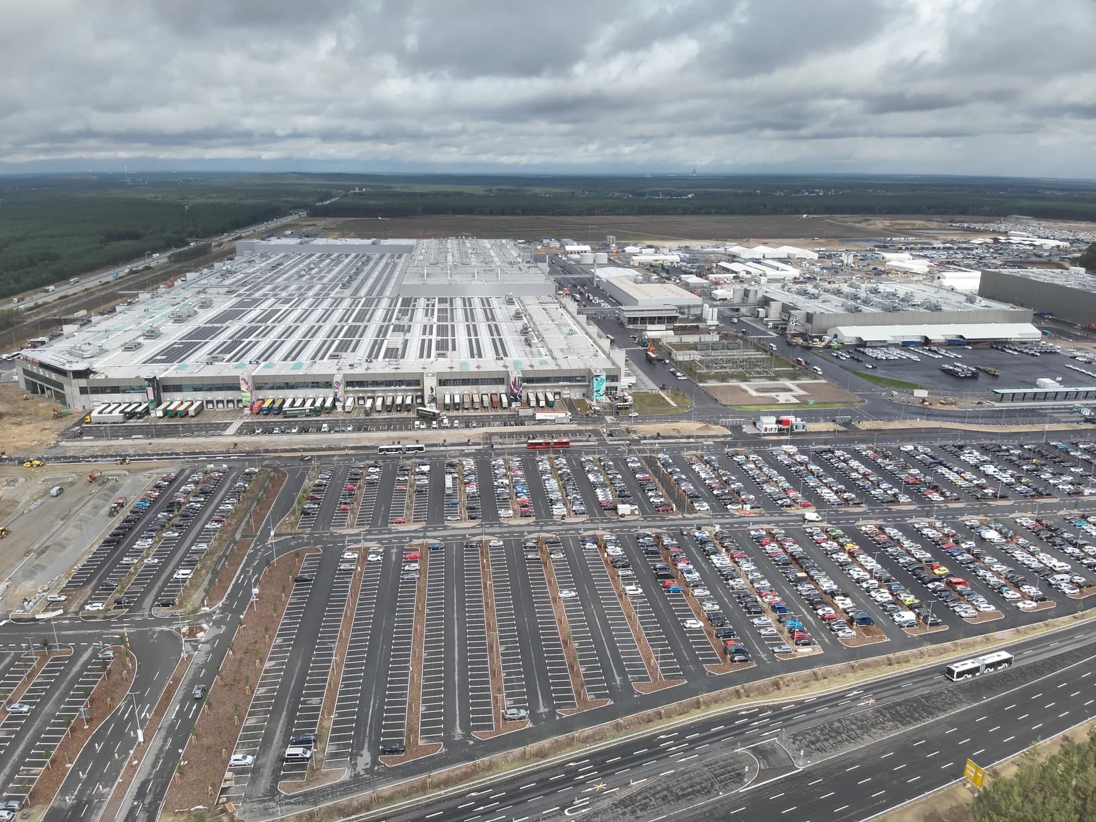 Aerial view of the Tesla Gigafactory production facility and parking lots under cloudy sky.