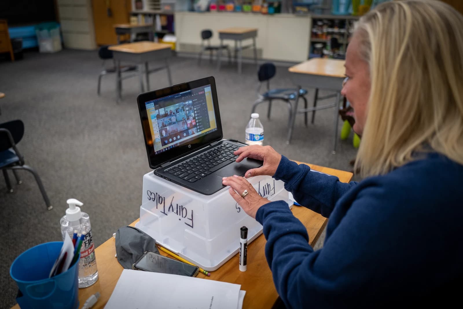 Teacher working on a laptop, conducting an online lesson in an empty classroom.