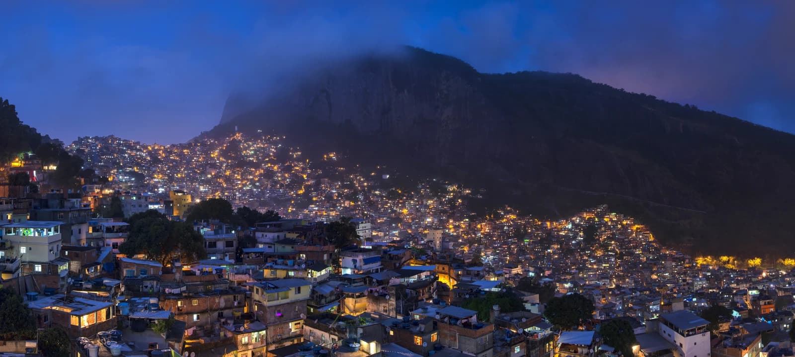 Rocinha favela at night in Rio de Janeiro, Brazil, with illuminated houses climbing a hillside.