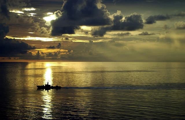 Republic of Singapore Navy warship silhouetted against a setting sun, leaving a wake.