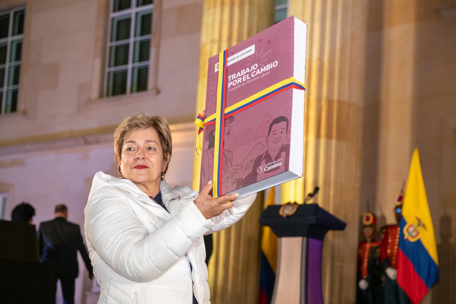Woman presenting a large book with the title "Trabajo por el Cambio: Proyecto de Reforma Laboral."