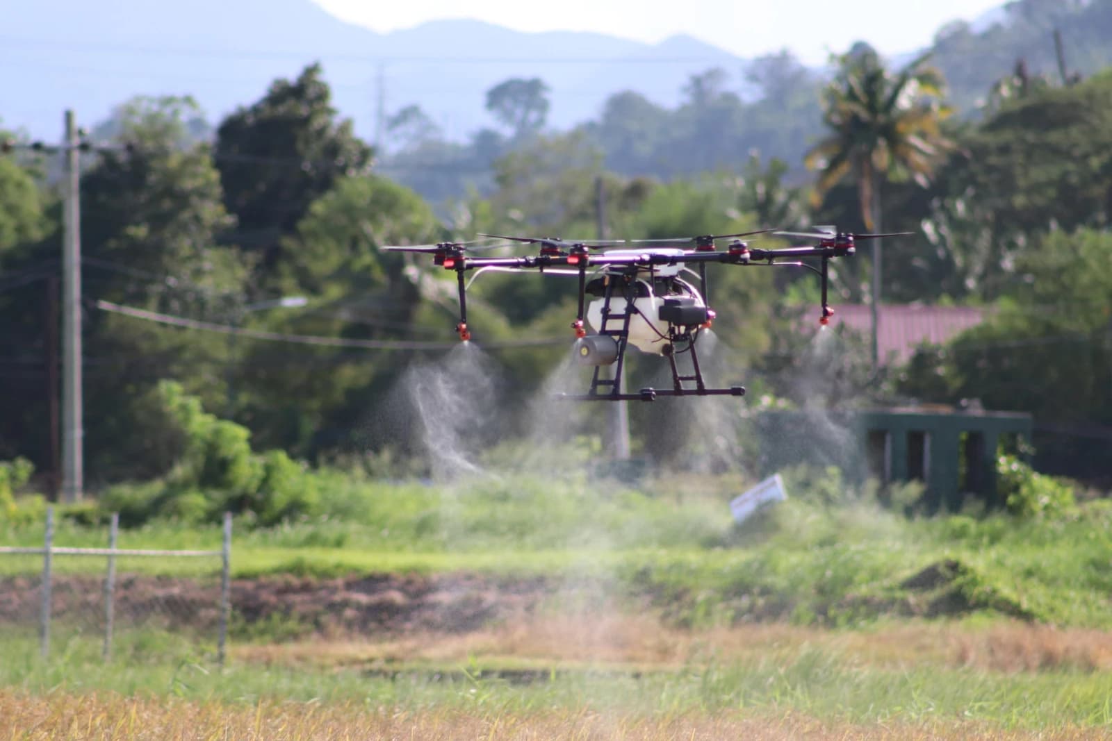 Agricultural drone hovering over a field, spraying liquid from nozzles.