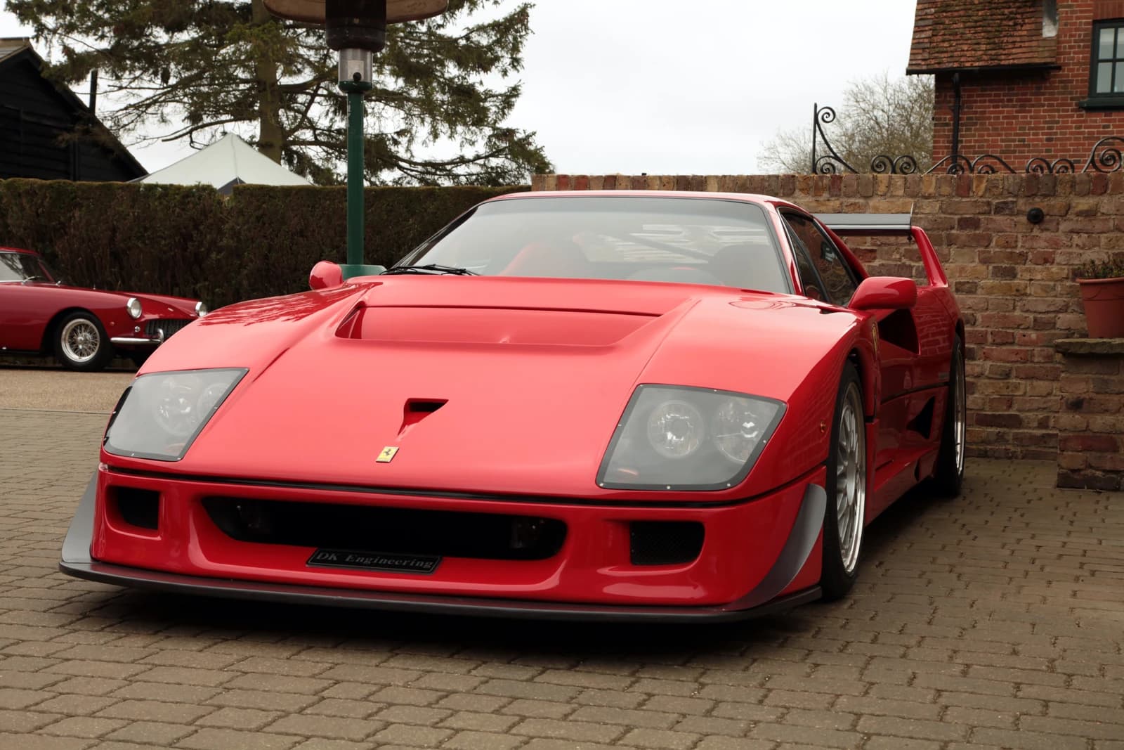 Red Ferrari F40 GT luxury sports car parked outdoors on a brick surface.