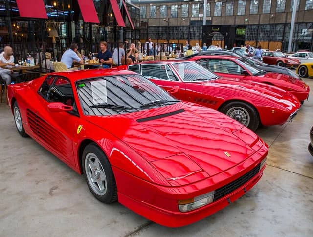 Red Ferrari Testarossa displayed indoors with several other classic red luxury cars.