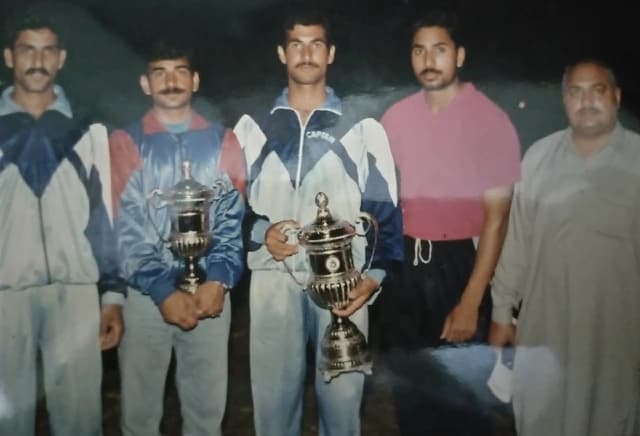 Suleman, a sports participant, holding a trophy with other men at an award ceremony.