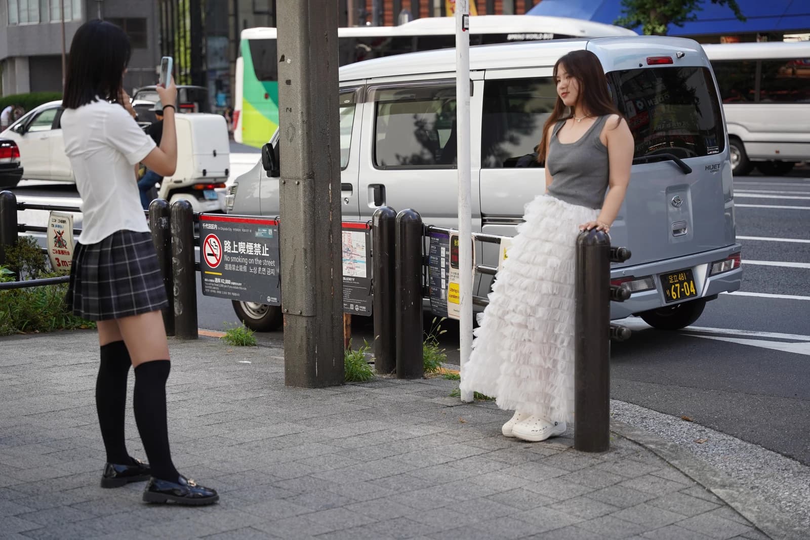 Two women, possibly Chinese tourists, taking photos on a street in Akihabara, Japan.