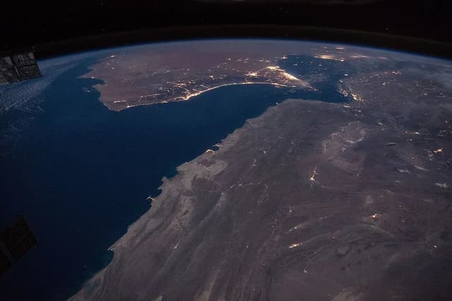 Aerial view of the Strait of Hormuz and Gulf of Oman at night with city lights.