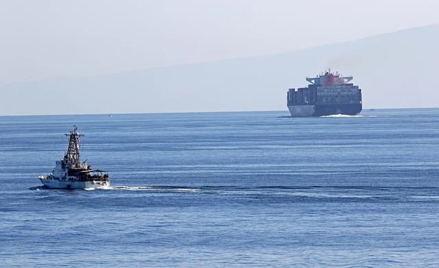 USCGC Aquidneck in the Strait of Hormuz, with a large container ship nearby.