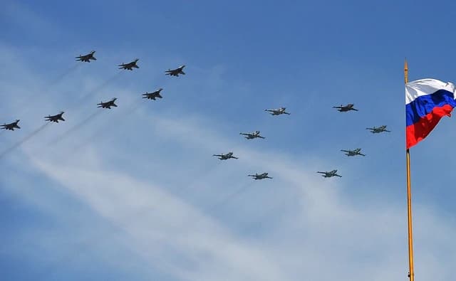 Russian Air Force jets flying in formation against a blue sky with the Russian flag.