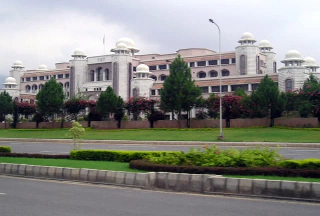 House of the Prime Minister of Pakistan, a large building with domed towers, viewed from a road.