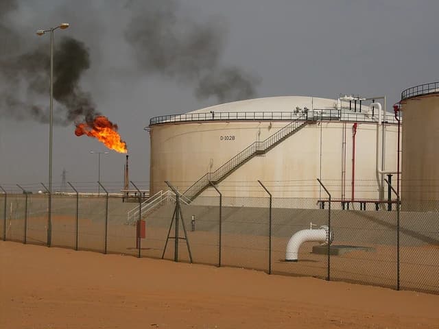 Gas flare burning at El Saharara oil field next to large storage tanks.