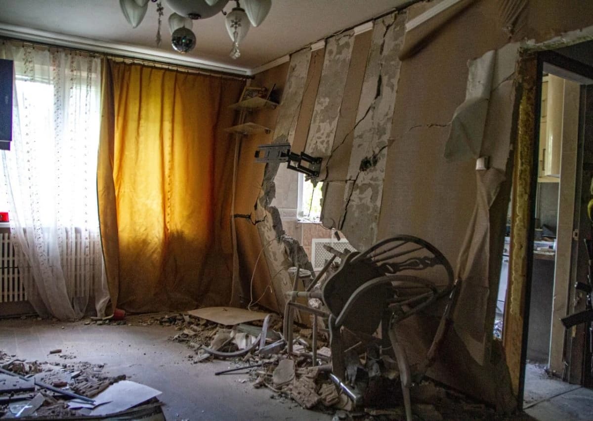 Interior of a damaged room with a large hole in the wall and debris on the floor.