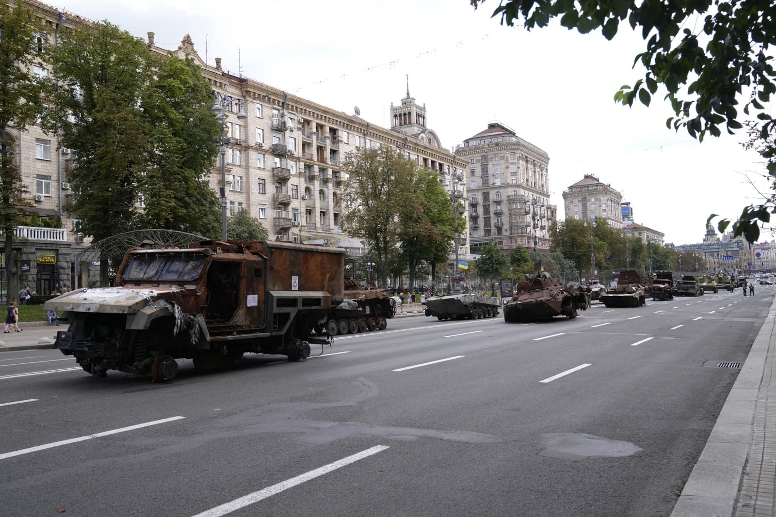 Several damaged military vehicles lined up on a street in Kyiv, Ukraine, with buildings in the background.