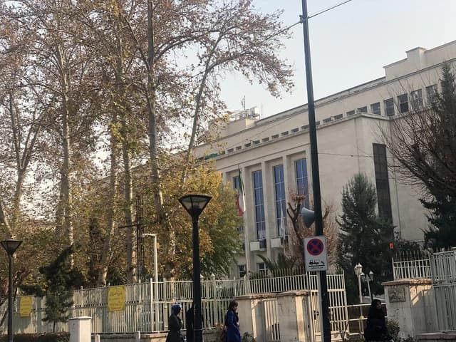 Exterior of the Ministry of Finance headquarters building in Iran with trees and a flag.