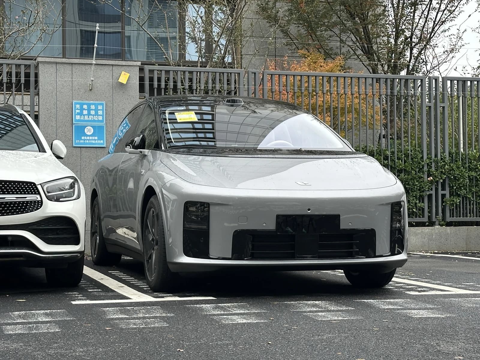 Li Auto vehicle parked in a lot next to a white Mercedes-Benz, a charging station sign nearby.