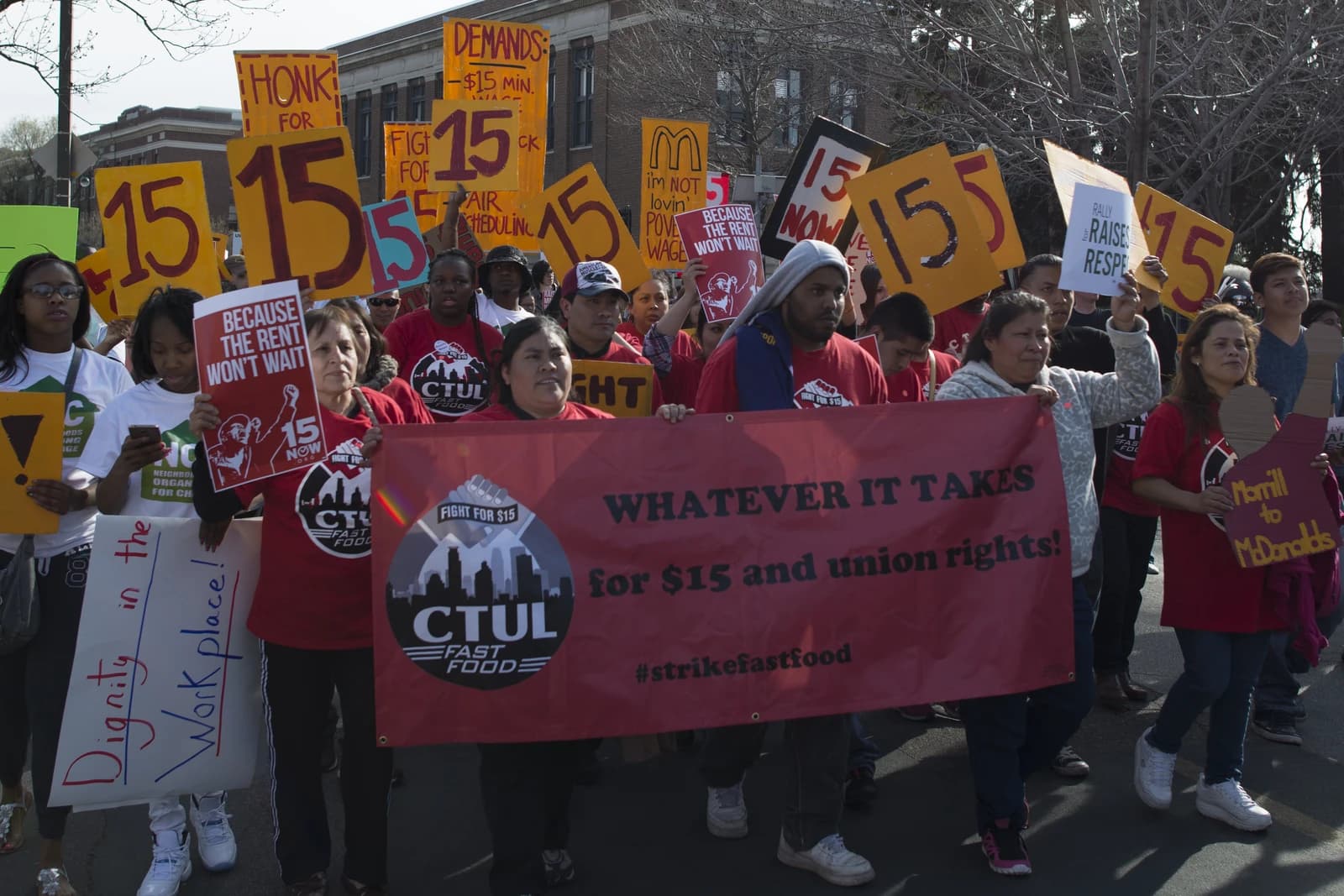 Protesters holding signs and a banner advocating for a $15 minimum wage.