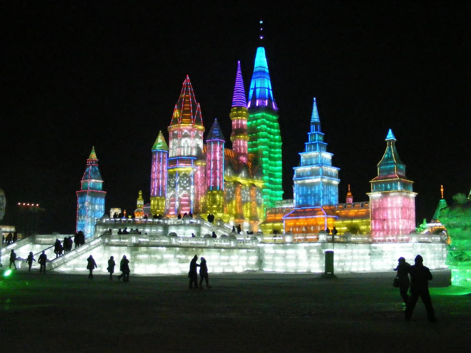People viewing colorful, illuminated ice sculptures at the Harbin Ice and Snow World festival.