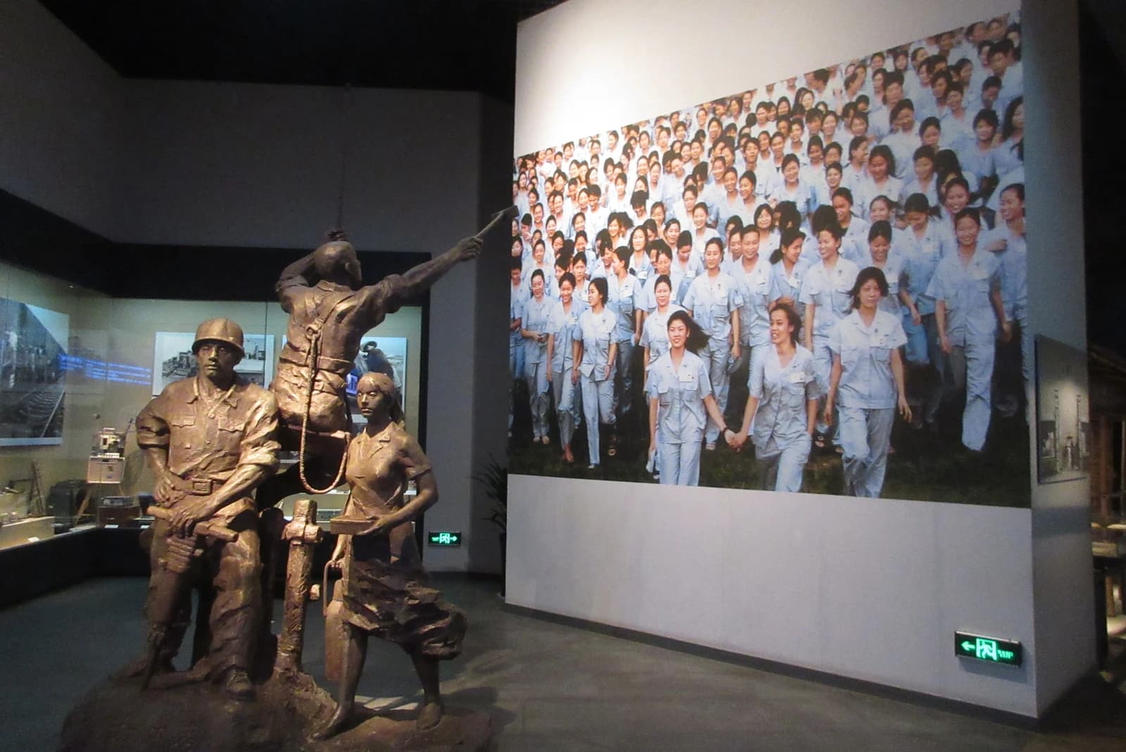 Exhibit at Shenzhen Museum showing a large photograph of many women factory workers and bronze statues.