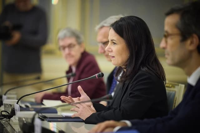 Annalena Baerbock, German Foreign Minister, speaking at a microphone at a table.