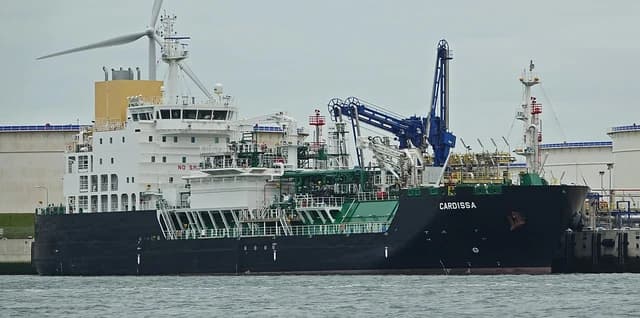 LNG tanker Cardissa docked in an industrial port facility, with a wind turbine visible.