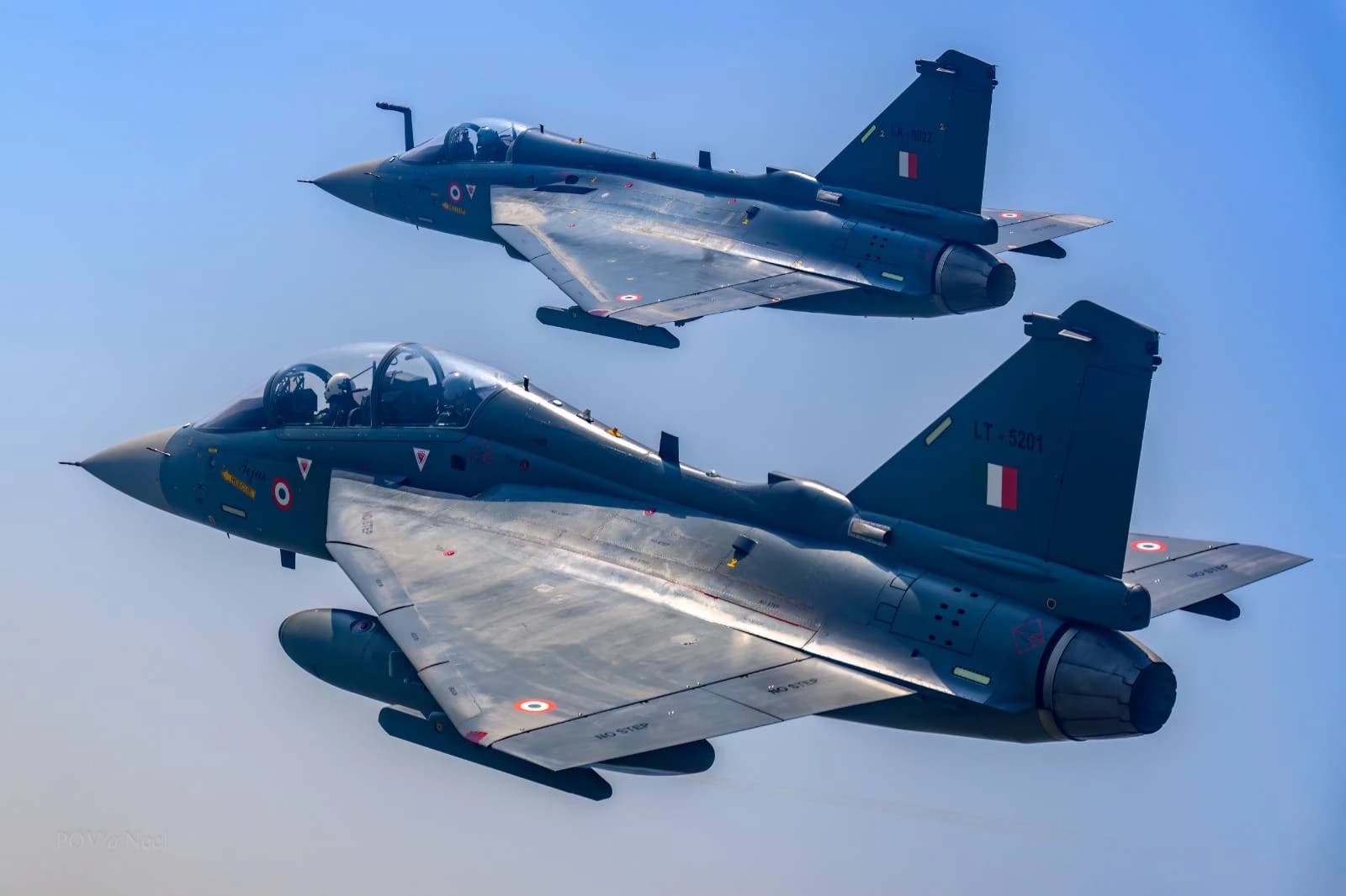 Two Indian Air Force Tejas fighter jets flying in formation against a clear blue sky.