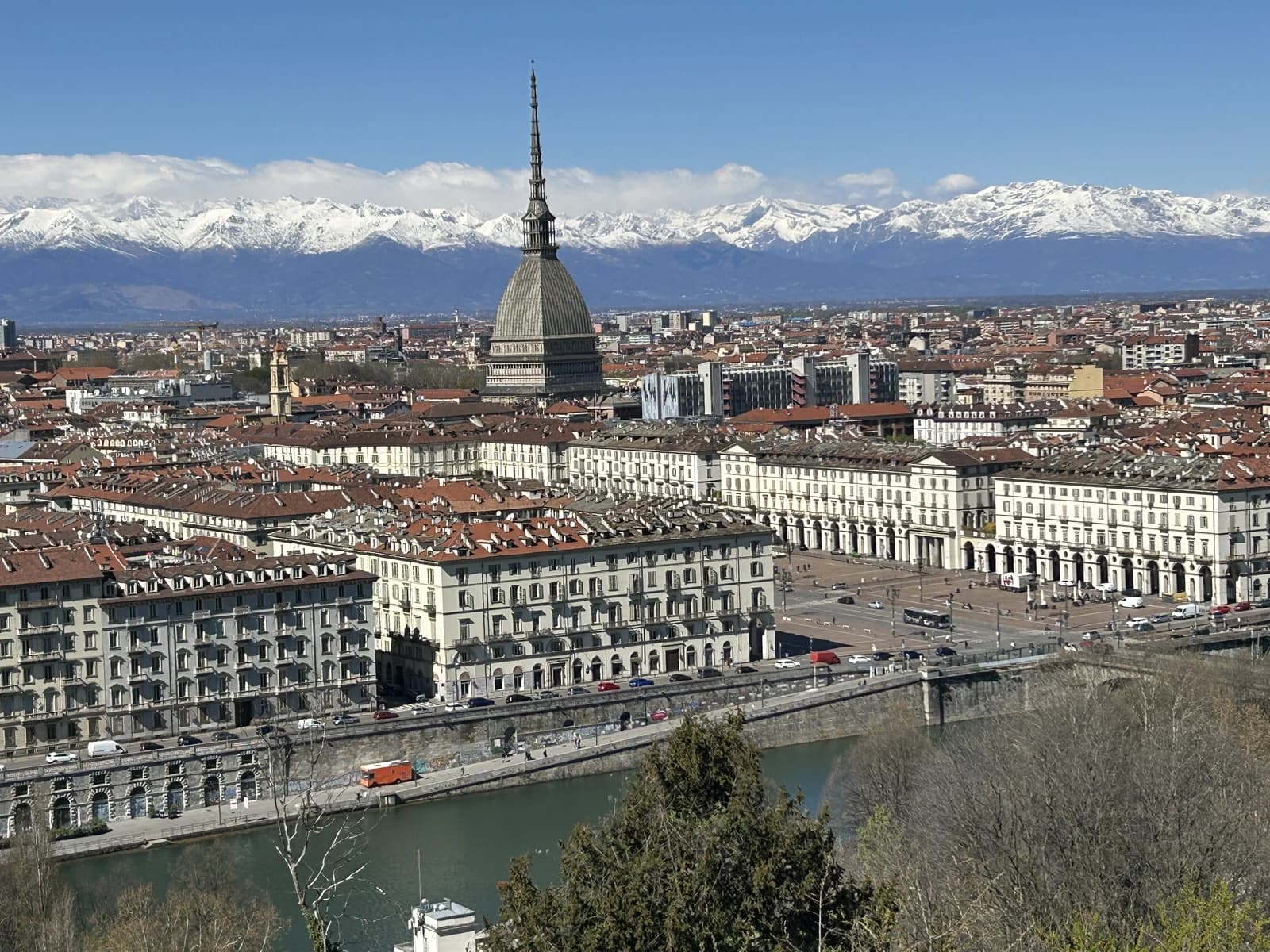 Turin skyline showing buildings, river, and snow-capped Alps mountains.