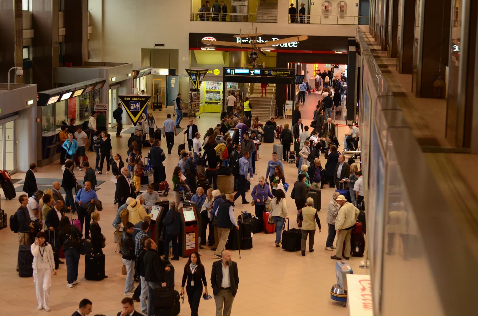 Many passengers with luggage in a busy airport terminal, viewed from above.