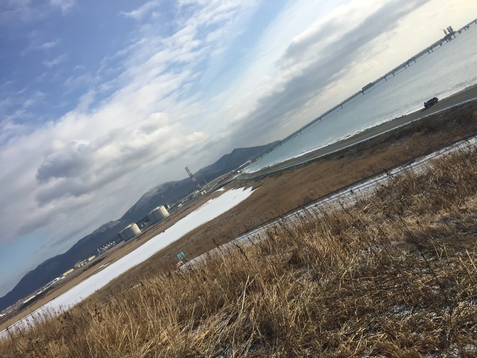 Port Prigorodnoye on Sakhalin Island, with industrial structures, a long pier, and mountains.