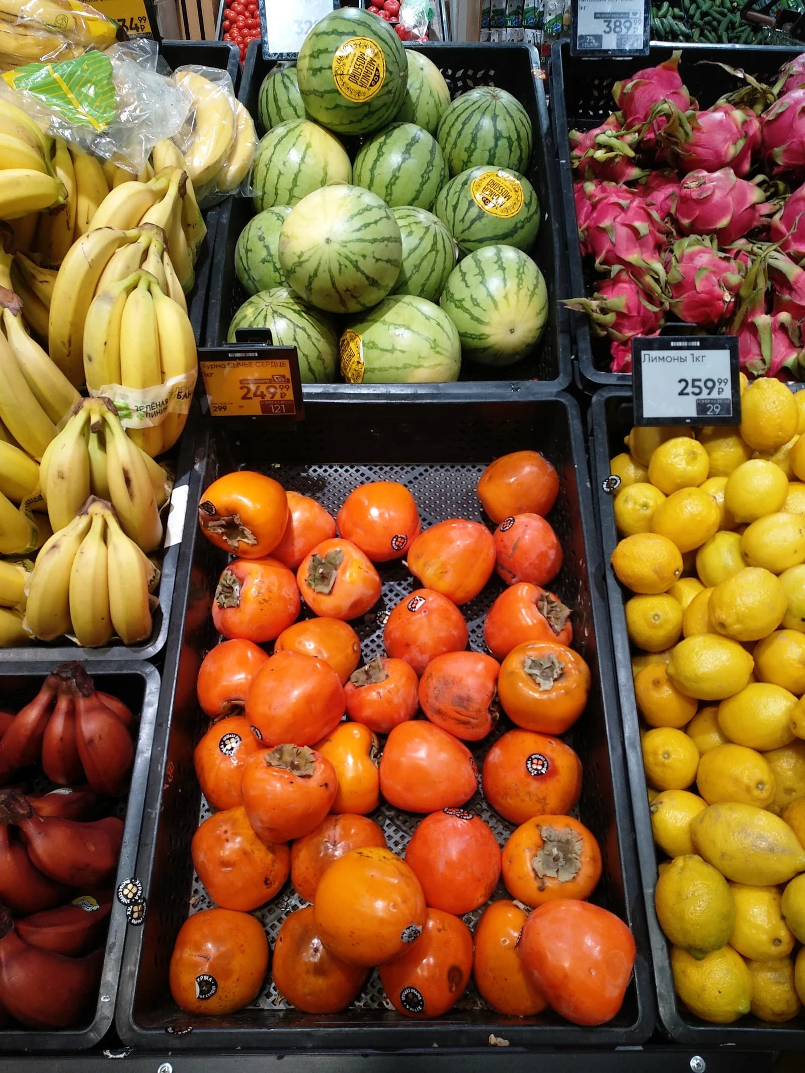 Close-up of bananas, watermelons, dragon fruit, persimmons, and lemons in a supermarket.