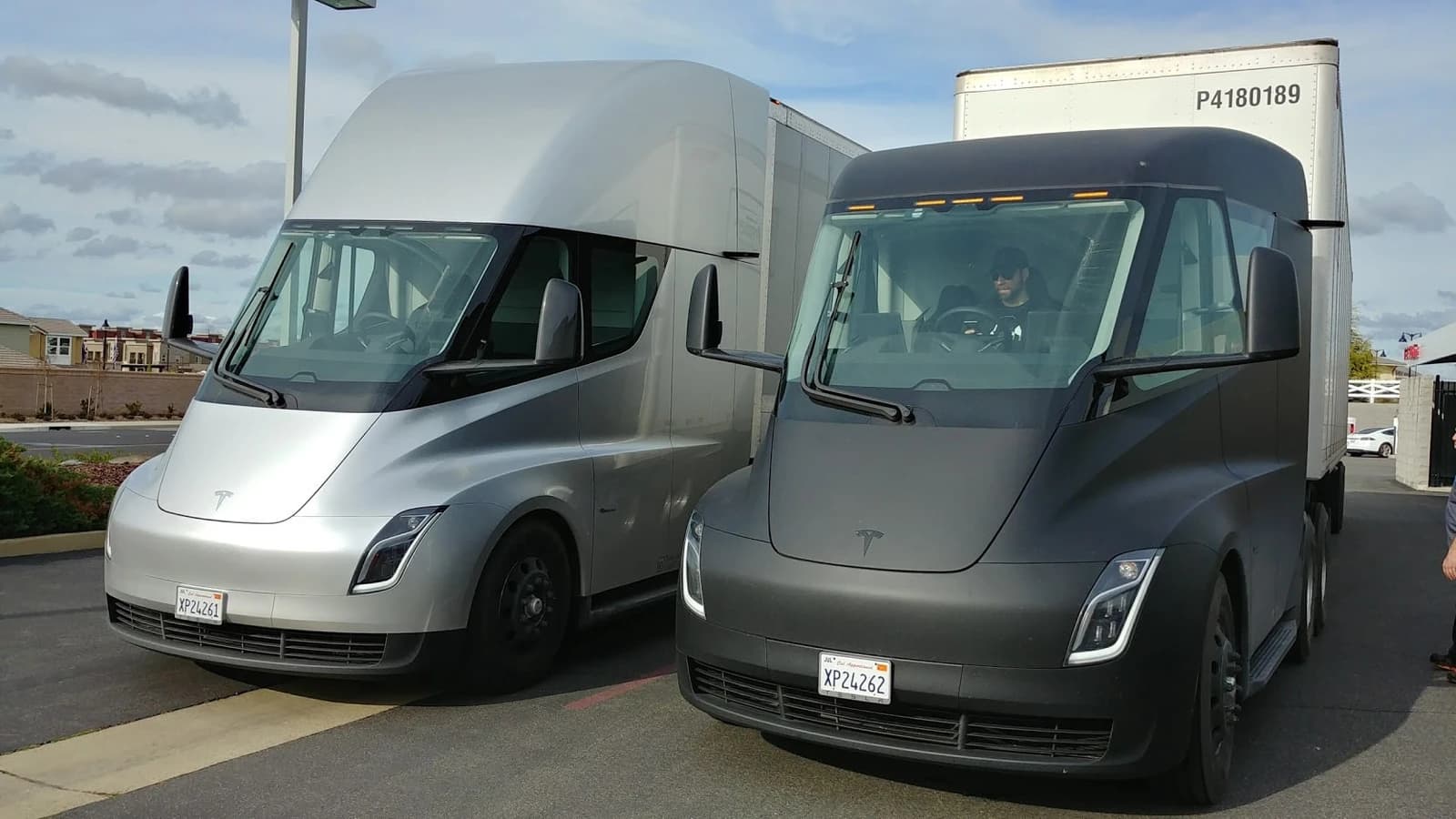 Two Tesla Semi electric trucks, one silver and one matte black, parked side by side.