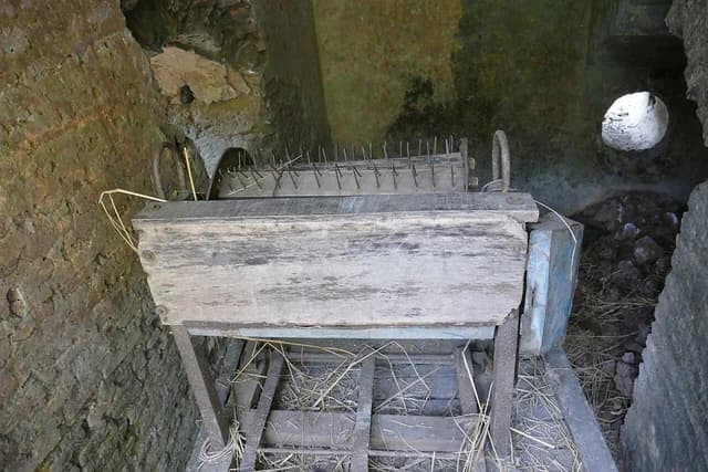 An old rice threshing machine with many spikes and wooden components.