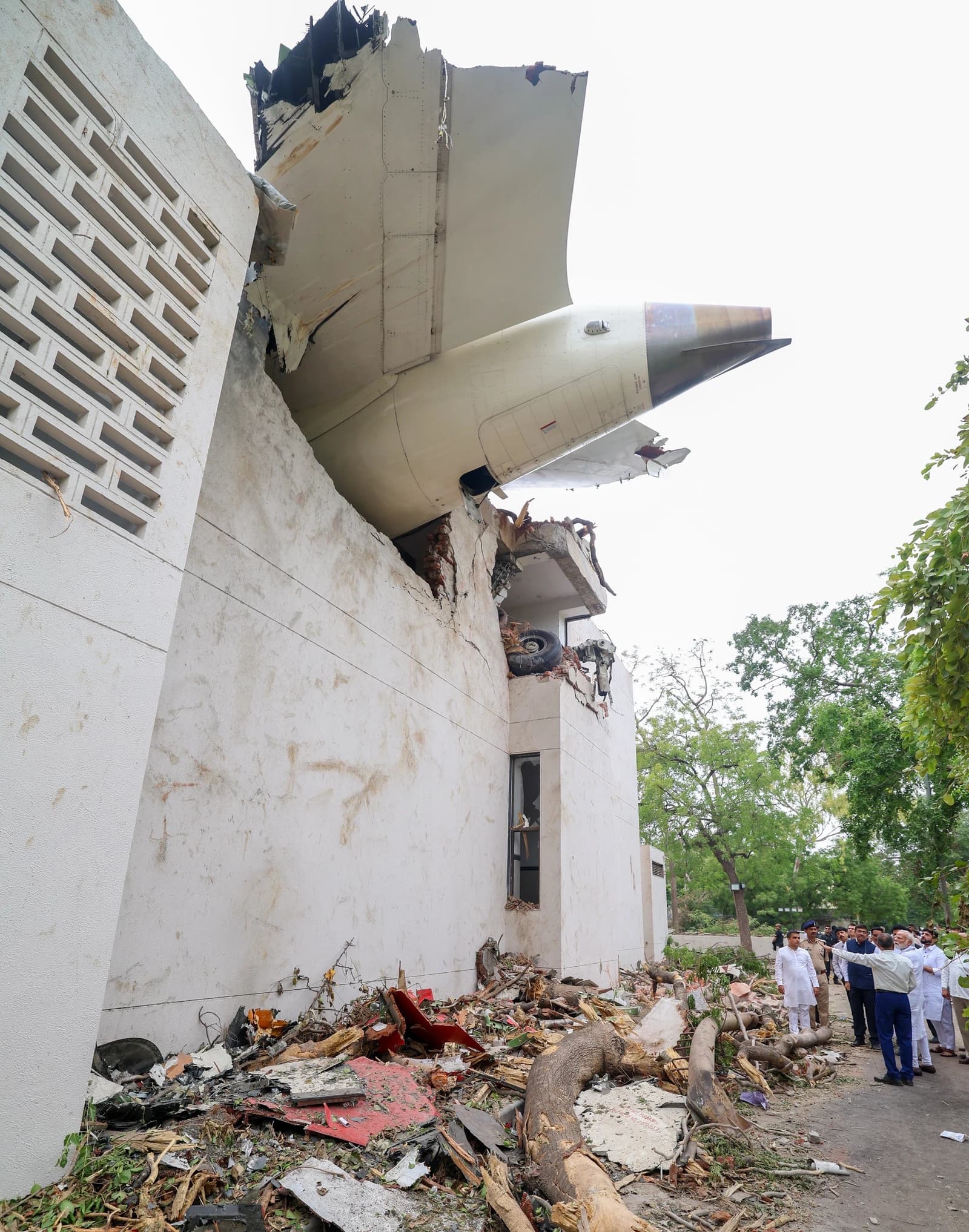 Portion of a white airplane tail and wing crashed into a white building, with debris on the ground.