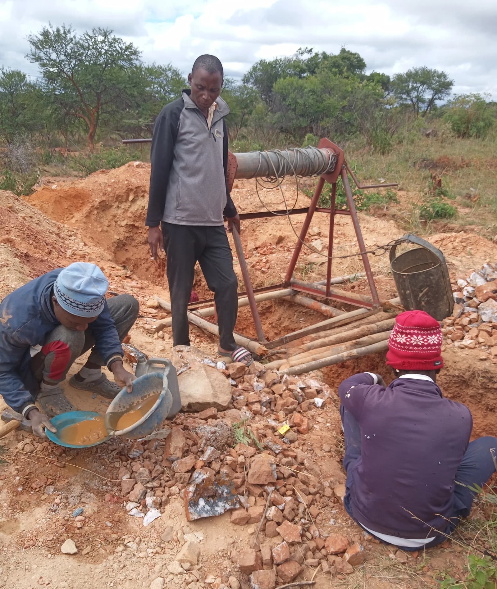 Three men working at an open-pit gold mine, one panning, one observing, one sitting.