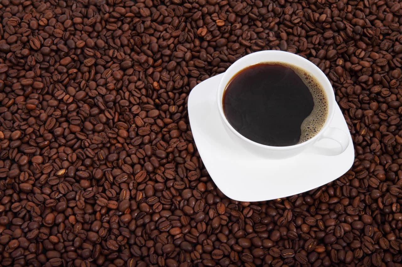White coffee cup with black coffee on a bed of roasted coffee beans.