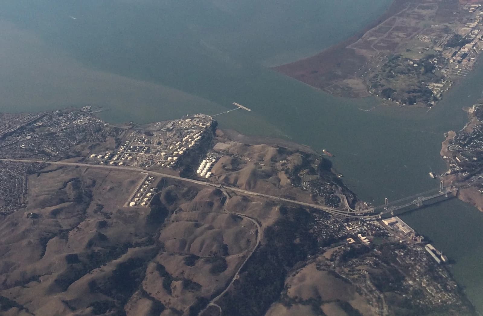 Aerial view of an oil refinery with numerous storage tanks near a body of water.
