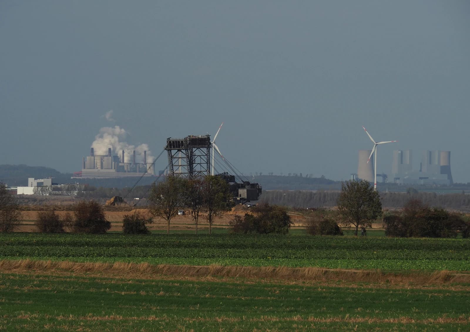 Lignite-fired power plants emitting smoke in the distance, with a lignite mine and wind turbines.