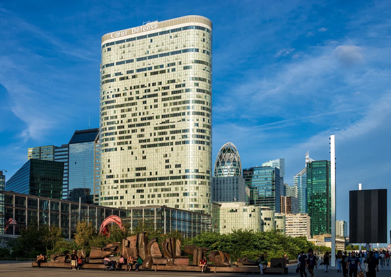 Cœur Défense skyscraper and surrounding buildings in La Défense, Paris, under a blue sky.