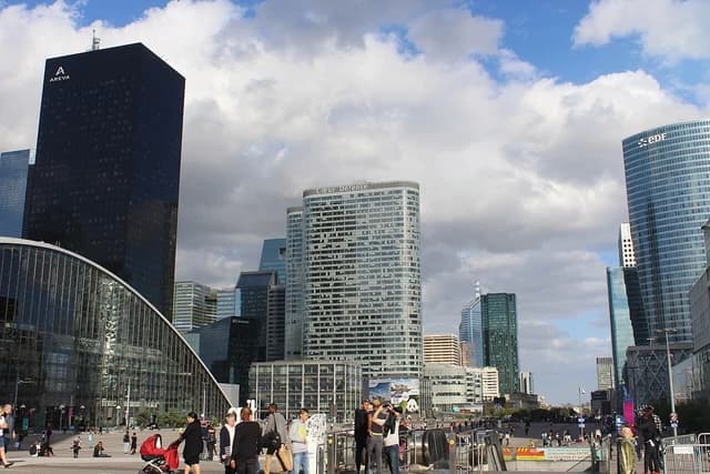 People walking on a plaza with modern skyscrapers and office buildings in La Défense, Paris.