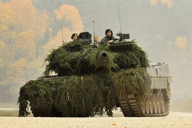 German Army Leopard 2 tank on a training ground with two crew members.