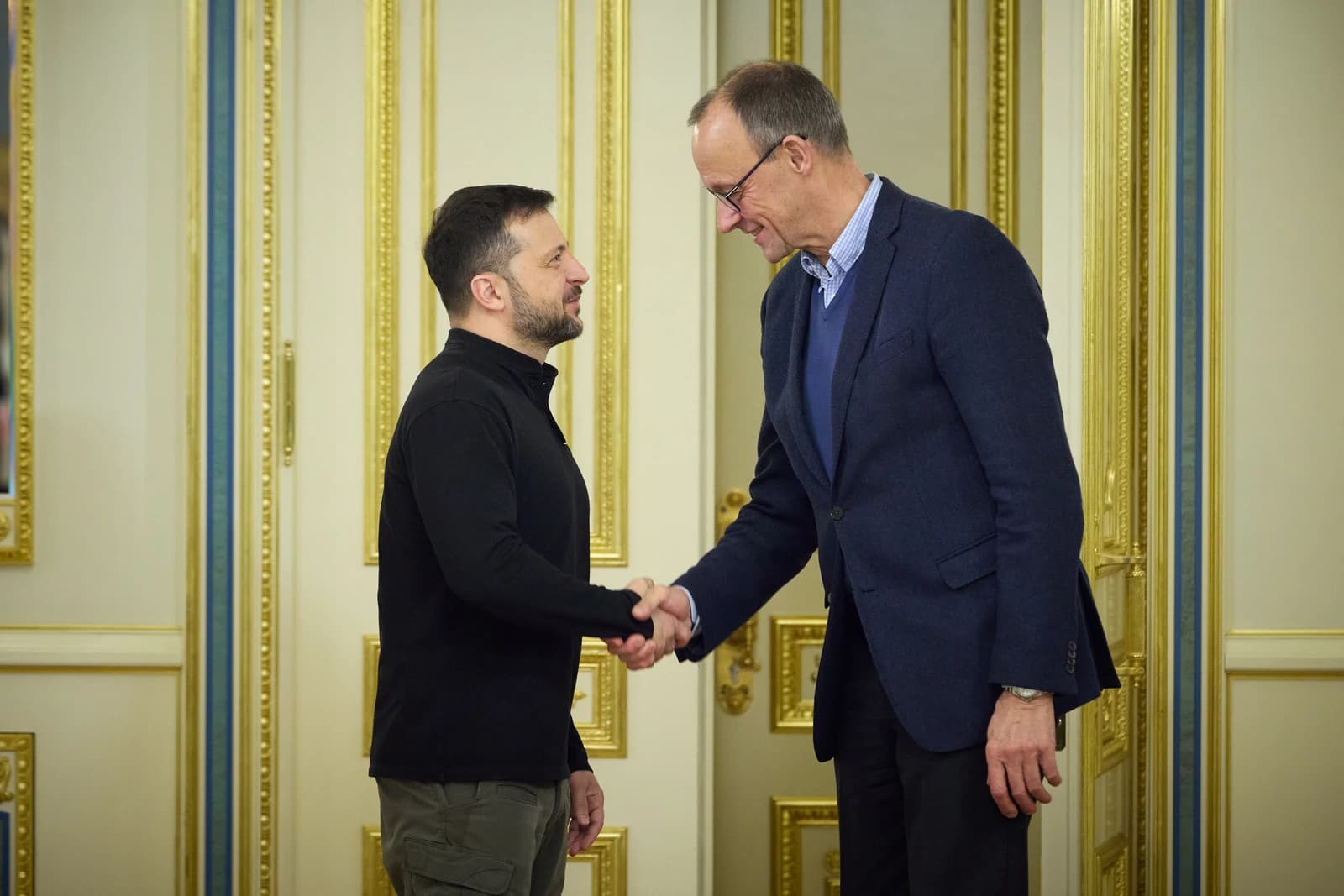 Ukrainian President Volodymyr Zelenskyy and German politician Friedrich Merz shaking hands in a formal room.