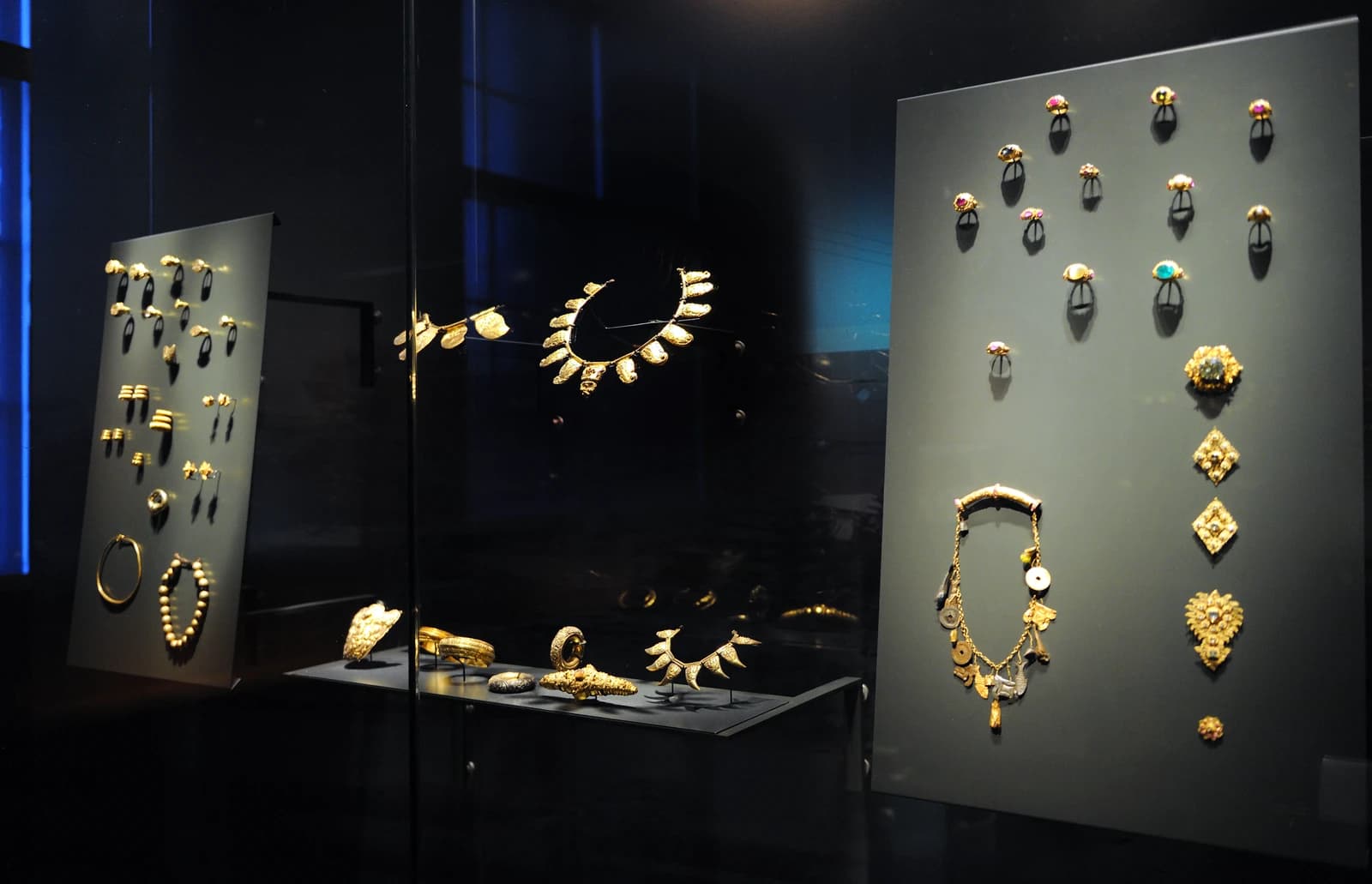 Indonesian gold jewelry pieces, including necklaces, rings, and bracelets, displayed in a dark room.